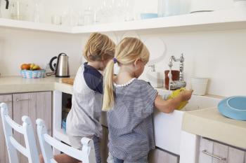 Brother and sister kneeling at sink to wash up in kitchen