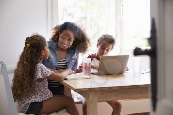 Mum sitting with kids at kitchen table, son using laptop