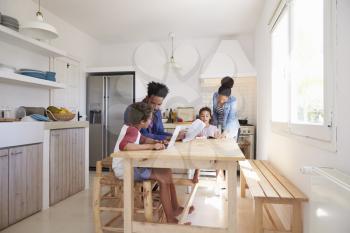 Mum and dad help their kids with homework at kitchen table
