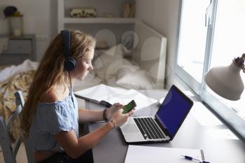 Girl wearing headphones using smartphone at desk in bedroom
