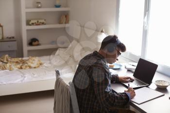 Teenage boy in headphones at desk in bedroom, elevated view