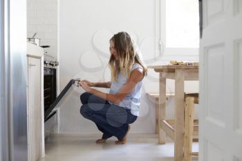 Woman squatting down in kitchen to look into the oven
