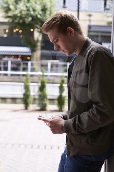 Man Sending Text Message On Mobile Phone In Urban Setting