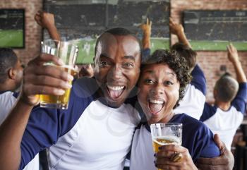 Portrait Of Couple Watching Game In Sports Bar On Screens