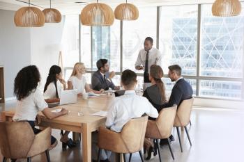 Businessman Stands To Address Meeting Around Board Table