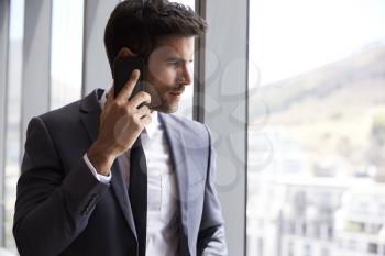 Businessman Making Phone Call Standing By Office Window