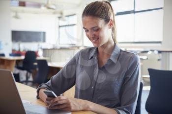 Happy young woman in office using smartphone