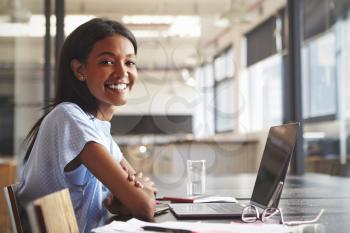 Young black woman in office using laptop smiling to camera