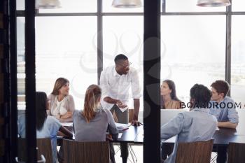 Man stands to address colleagues at a meeting in a boardroom