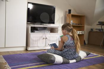 Girl Watches Television And Using Digital Tablet In Playroom