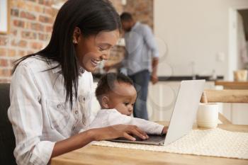 Mother And Baby Daughter Use Laptop As Father Prepares Meal