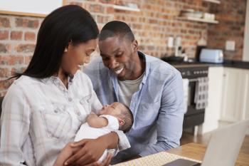 Mother Working On Laptop Holds Newborn Son With Father