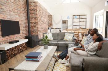Couple Sit On Sofa In Open Plan Lounge Watching Television