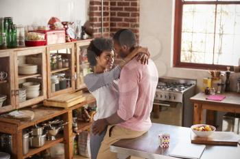Mixed race couple sit embracing in kitchen, high angle
