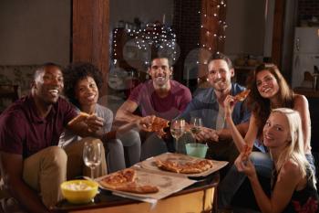 Young adults eating pizza at a party look to camera