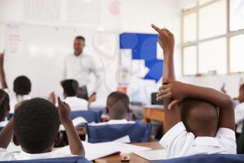 Kids raising hands to answer teacher at an elementary school lesson