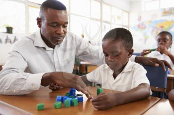 Teacher helping elementary school boy counting with blocks