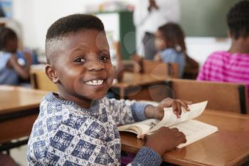 Boy at desk smiling to camera in an elementary school lesson
