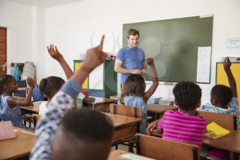 Kids raising hands to teacher in an elementary school class