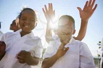Elementary school kids in playground waving to camera