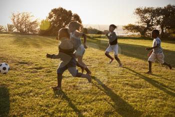 Four elementary school kids playing football in a field