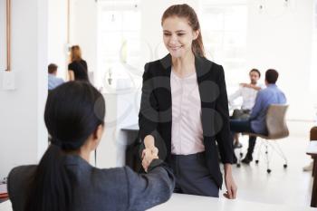 Two women shaking hands at a meeting in an open plan office