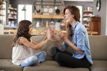 Mother And Daughter Sitting On Sofa Playing Clapping Game