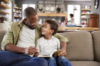 Father And Son Sitting On Sofa In Lounge Reading Book Together