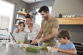 Family In Kitchen Following Recipe On Digital Tablet Together