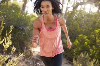 Determined young black woman jogging in a forest, close up