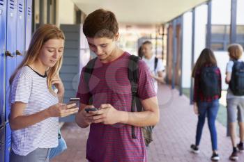 Two friends talking and using phones in school corridor