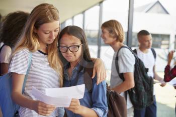 Two girls sharing exam results in school corridor