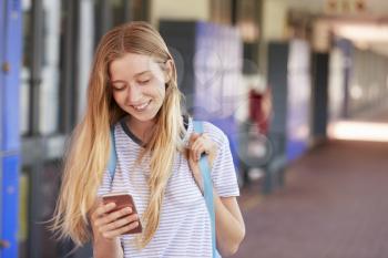 Happy teenage girl using smartphone in school corridor