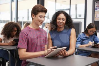 Teacher helping teenage schoolboy with tablet computer
