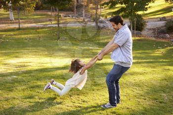 Father Swinging Daughter By Her Arms In Park