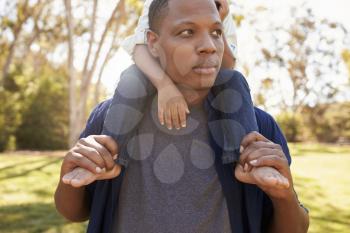 Close Up Of Father Carrying Son On Shoulders Walking In Park