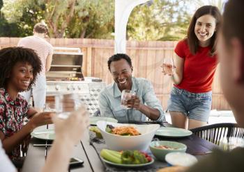 Young adult friends sitting outdoors and barbecuing