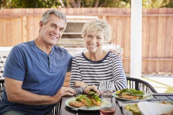 Senior white couple sit at lunch in garden looking to camera