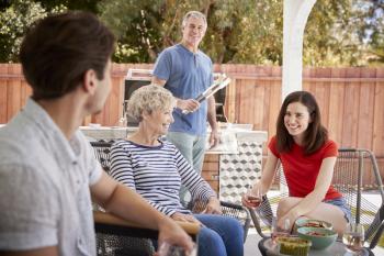 Senior couple and adult children barbecuing outside house