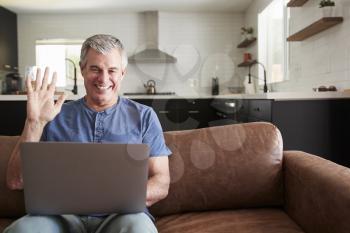 Senior man video calling on laptop at home, waving to screen