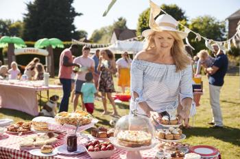 Mature Woman Serving On Cake Stall At Busy Summer Garden Fete