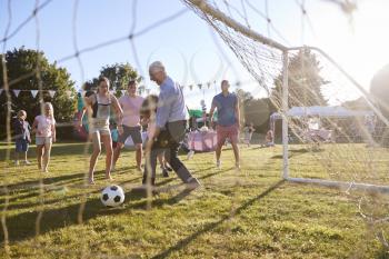 Children Playing Football Match With Father And Grandfather At Summer Garden Fete