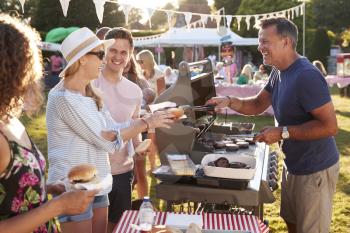 Man Serving On Barbeque Stall At Summer Garden Fete