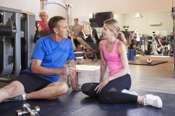 Senior Man Discussing Exercise Program With Male Personal Trainer In Gym