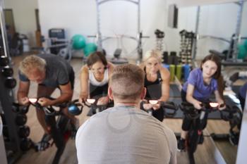 Rear View Of Male Trainer Taking Spin Class In Gym
