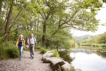 Senior Couple Hiking Along Path By River In UK Lake District