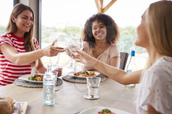 Multi ethnic group of three young adult women making a toast,celebrating with wine glasses during a dinner party