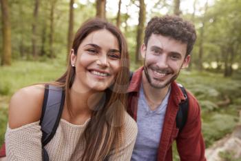 A young adult couple smiling to camera during a hike in a forest, close up portrait