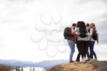 A group of five mixed race young adult friends embrace after arriving at the summit during mountain hike, close up