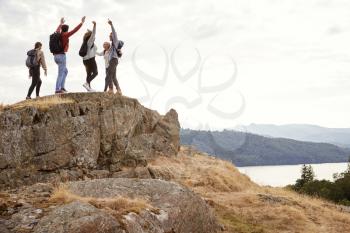 A group of five happy young adult friends cheer with their arms in the air at the summit during mountain hike